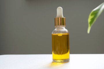 Oil serum in glass bottle with pipette. Yellow essence and green leaf