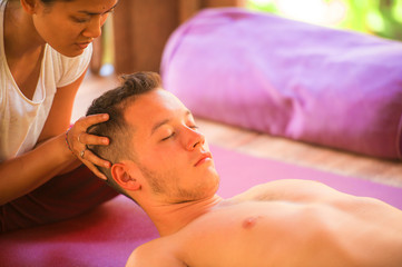 Obraz na płótnie Canvas young beautiful and exotic Asian Thai therapist woman giving traditional head and facial Balinese massage to Caucasian man at alternative medicine healing spa