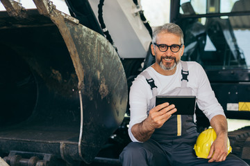 worker sitting on excavator using tablet