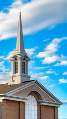 Vertical Exterior of a beautiful church with a white steeple against cloudy blue sky