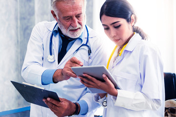 Senior male doctor using tablet computer while discussing with another doctor at the hospital....