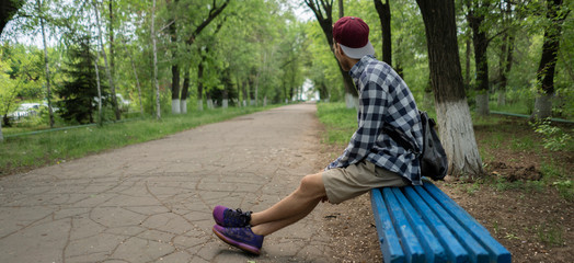a male sitting on the bench in the city park alley during summers