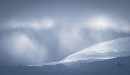 Sunlight shining through the cloudcover over the snow covered mountains in Sarek National Park.  Lapland, Sweden.