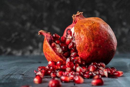 a large opened  pomegranate fruit with many seeds grains fall pouring out of it s