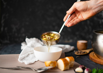 chefs hand pour fresh hot soup in a white empty bowl, food preparations