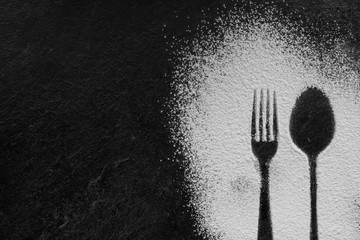 Spoon and fork silhouette made with flour on dark texture background