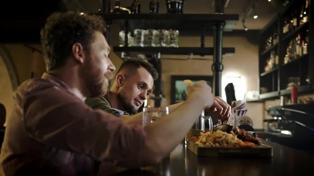 Cheerful friends drinking draft beer and eating snacks in a pub