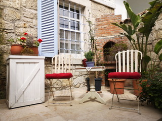 Gartenmöbel auf der Terrasse vor einem Landhaus aus Naturstein in Beige und Naturfarben im Sommer...