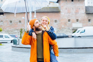 Positive bearded man with transparent umbrella and hiis girlfriend in bright wear complementary...