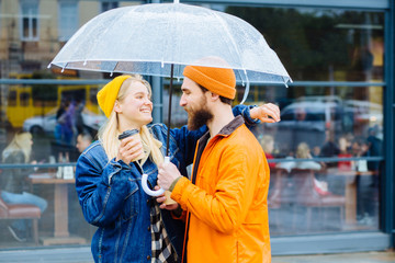 Happy hipster couple hugging under trensparent umbrella in the city.