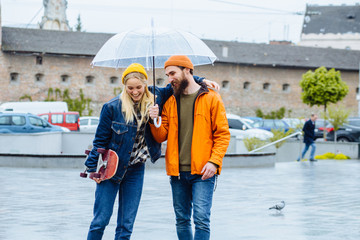 Portrait of lovely hipster couple walking hugging together under transparent umbrella laughing...