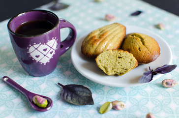 Pistachio madeleines in white plate decorated with pistachios and fresh basil 