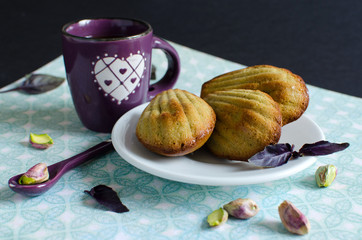 Pistachio madeleines in white plate decorated with pistachios and fresh basil