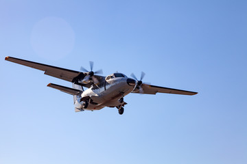 A small aircraft for the transport of passengers and paratroopers lands in a field on a landing strip with grass under a blue sky above the trees on a clear cloudless day. Air patrol.