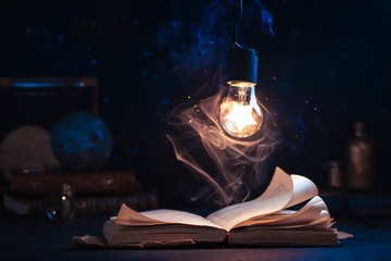 An open book with lighting by a star inside a lightbulb. Night reading conceptual still life with...