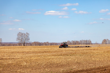 Fototapeta na wymiar Red tractor with a trailed plow for mowing and weeding fields for the agro-industry of yellow color under the blue sky, a clear spring day. Preparation for planting crops rural technology. Farming.