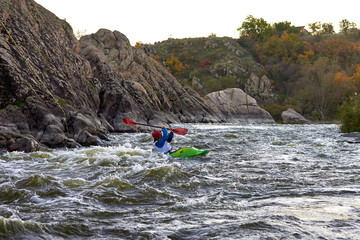 Man jedi in green kayak fights with rapids of fast mountain river among the rocks. Whitewater kayaking, extreme water sport.