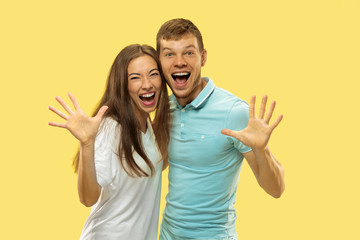 Beautiful young couple's half-length portrait on yellow studio background. Woman and man in shirts caddling and show the gesture of Hello. Facial expression, human emotions concept. Trendy colors.