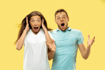 Beautiful young couple's half-length portrait on yellow studio background. Woman and man in shirts astonished or shocked of something. Facial expression, human emotions concept. Trendy colors.