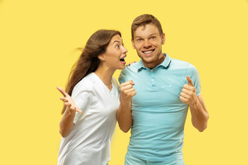 Naklejka premium Beautiful young couple's half-length portrait on yellow studio background. Woman and man in shirts celebrating and showing the sign of OK. Facial expression, human emotions concept. Trendy colors.