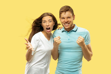 Fototapeta premium Beautiful young couple's half-length portrait on yellow studio background. Woman and man in shirts celebrating something and happy. Facial expression, human emotions concept. Trendy colors.