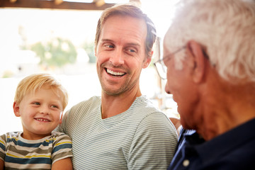 Father With Adult Son And Teenage Grandson Relaxing On Sofa And Talking At Home