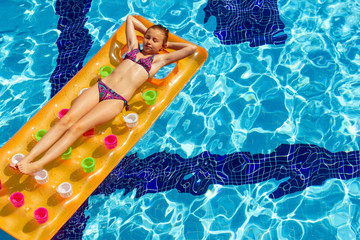 The girl relaxes on an orange inflatable mattress in the pool, taking air baths.