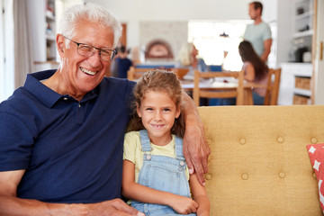 Portrait Of Grandfather Sitting With Granddaughter On Sofa At Home