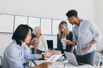 Busy office workers arguing about report and analysing documents. Indoor portrait of confused international developers using laptops during meeting.