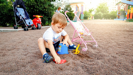 Cute 3 years old little boy playing on the children playground in park. Toddler digging sand with...