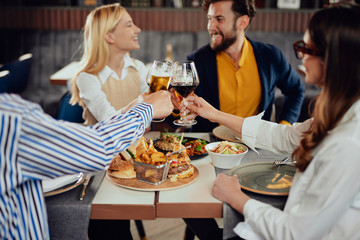 Four happy muliethnic freinds dressed smart casual cheering with alcohol while sitting at restaurant.
