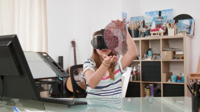 Young girl doing her homework and learning about human anatomy bu displaying a virtual brain in front of her. She is wearing a VR headset. The future of education and AI