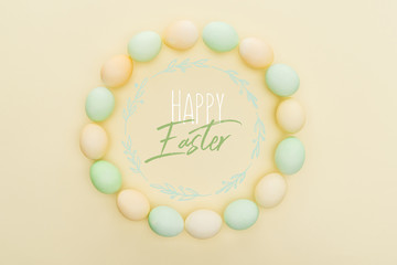 top view of round frame made of painted chicken eggs on light yellow background with happy Easter lettering inside