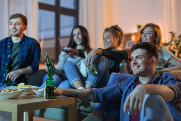 friendship and leisure concept - happy friends with non-alcoholic drinks watching tv at home in...