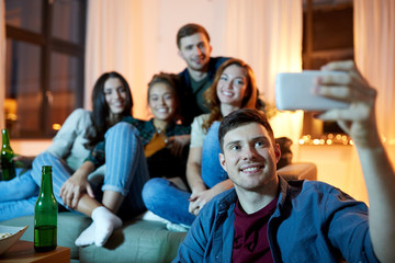 friendship, people, technology and entertainment concept - happy friends with non-alcoholic drinks taking selfie by smartphone at home in evening