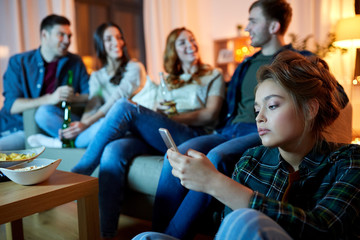technology, internet addiction and people concept - sad young woman with smartphone at home friends...