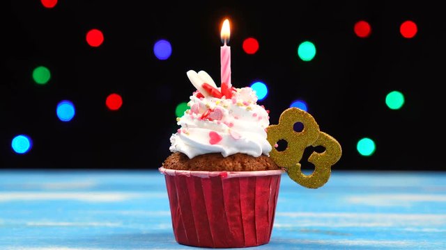 Delicious birthday cupcake with burning candle and number 83 on multicolored blurred lights background