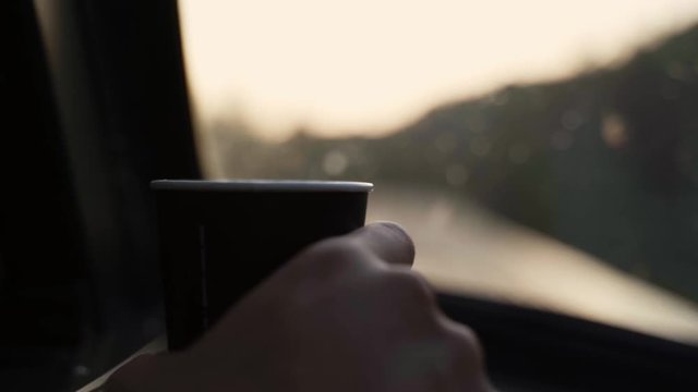 Someone holding a cup of coffee in front of a train window in movement.