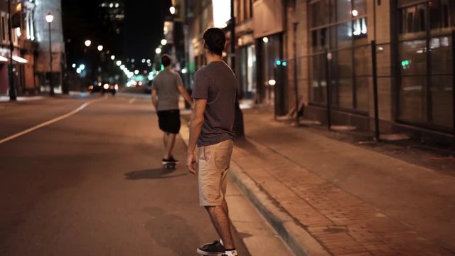 Two men skateboarding seen from behind in the streets of Halifax, Nova Scotia, Canada - night time.