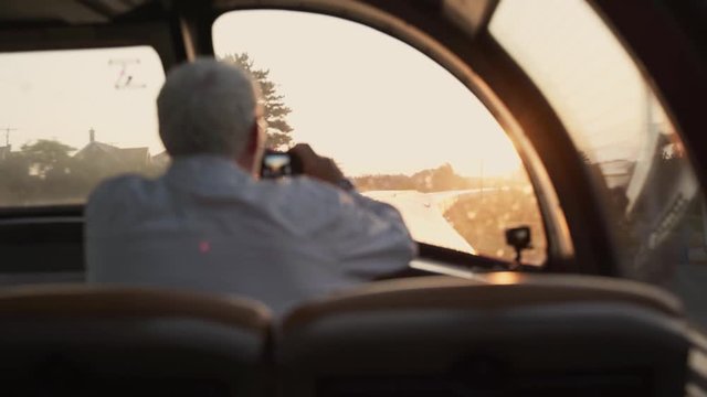 A senior / old man taking pictures / photos in front of a window of a sightseeing train - panoramic view during sunrise.