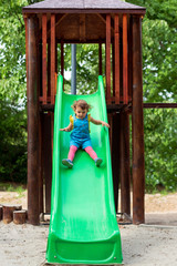 Cute girl chuting down slide at playground.