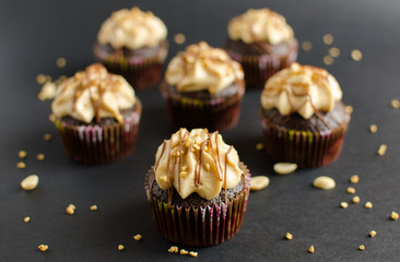 Set of chocolate cupcakes with peanut cream and chocolate sauce decorated with peanut on black background