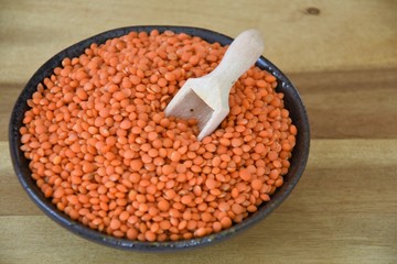boiled red lentils in a black bowl and scattered on a wooden board with a wooden spoon