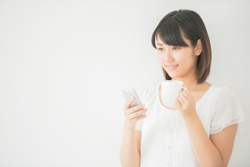 コーヒーカップを持ちスマートフォンを操作する女性