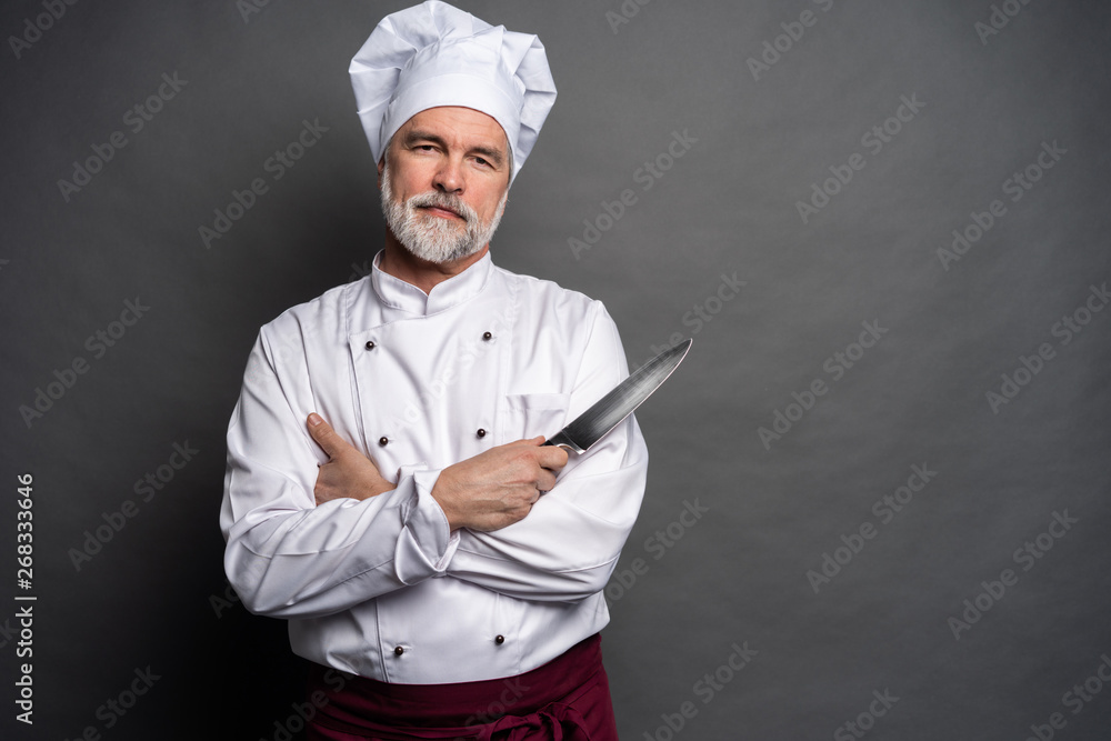 Wall mural portrait of a mature chef cook holding knifes isolated on a black background.