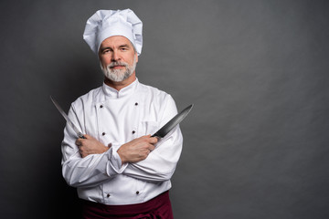 Portrait of a mature chef cook holding knifes isolated on a black background.