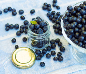 Full jar of fresh blueberries berrywith green leaf on top, with berries laying around on linen textile on table with glass dessert vase nearby, copy space, closeup