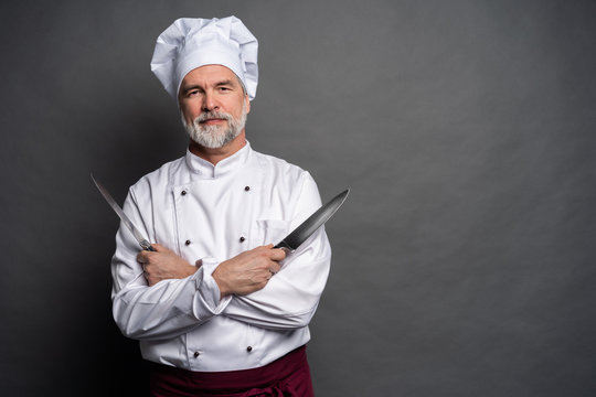 Portrait of a mature chef cook holding knifes isolated on a black background.