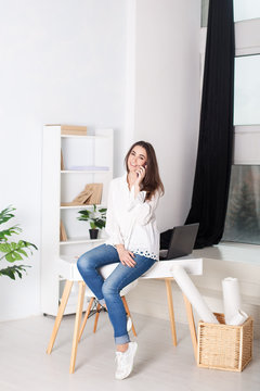 Business vumen. Young girl working in the office. The girl calls on the phone and sits on the table. Calling customers of the company.  Positive young manager working on business project in office. 