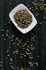 Green peppercorns in white bowl on wooden background